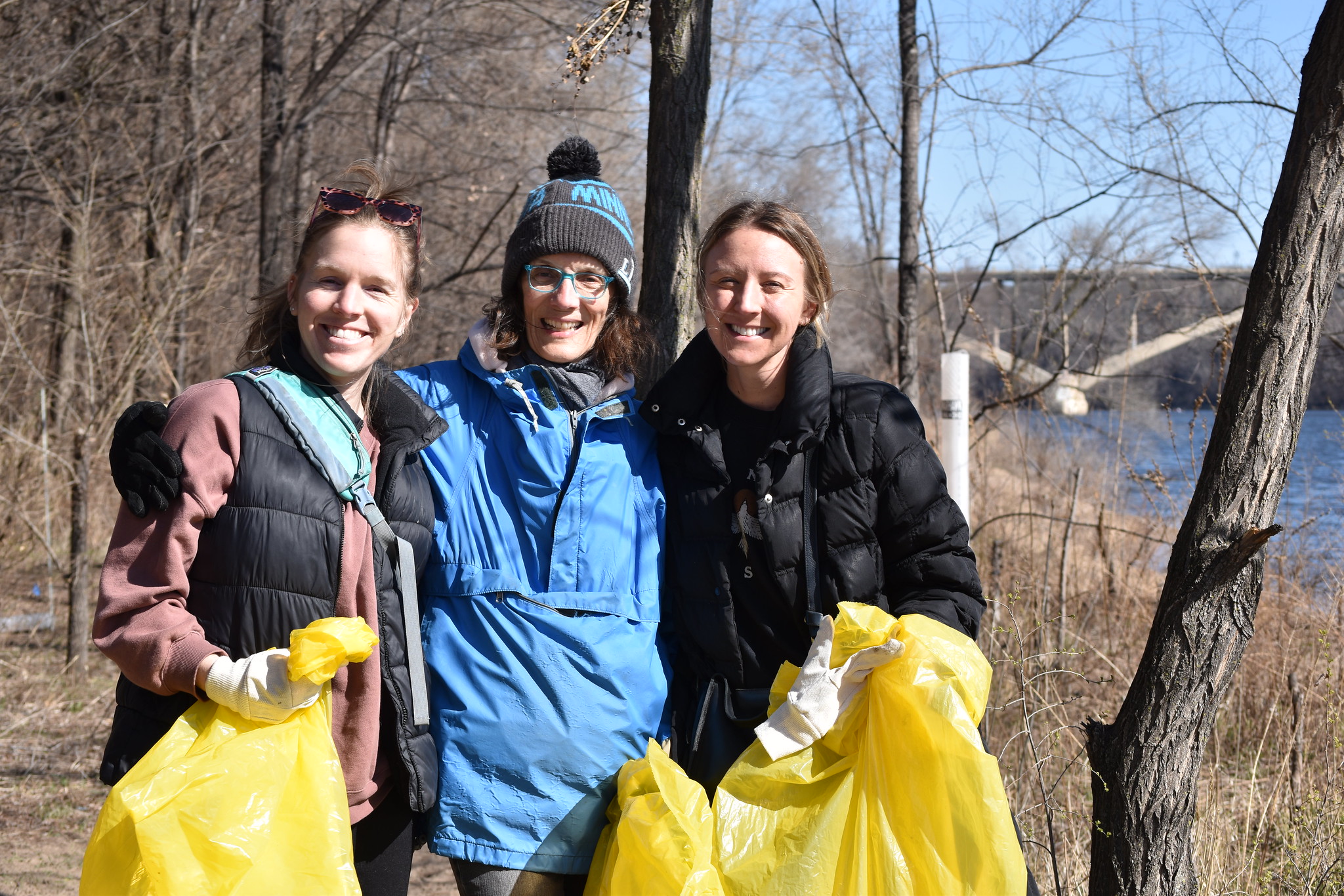 Three volunteers with cleanup bags by the river