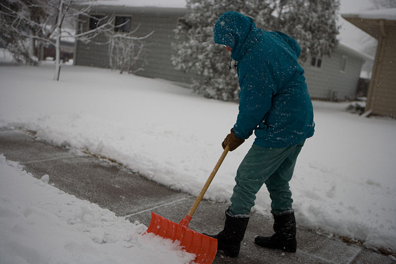 A person in a coat shovels snow off a sidewalk.