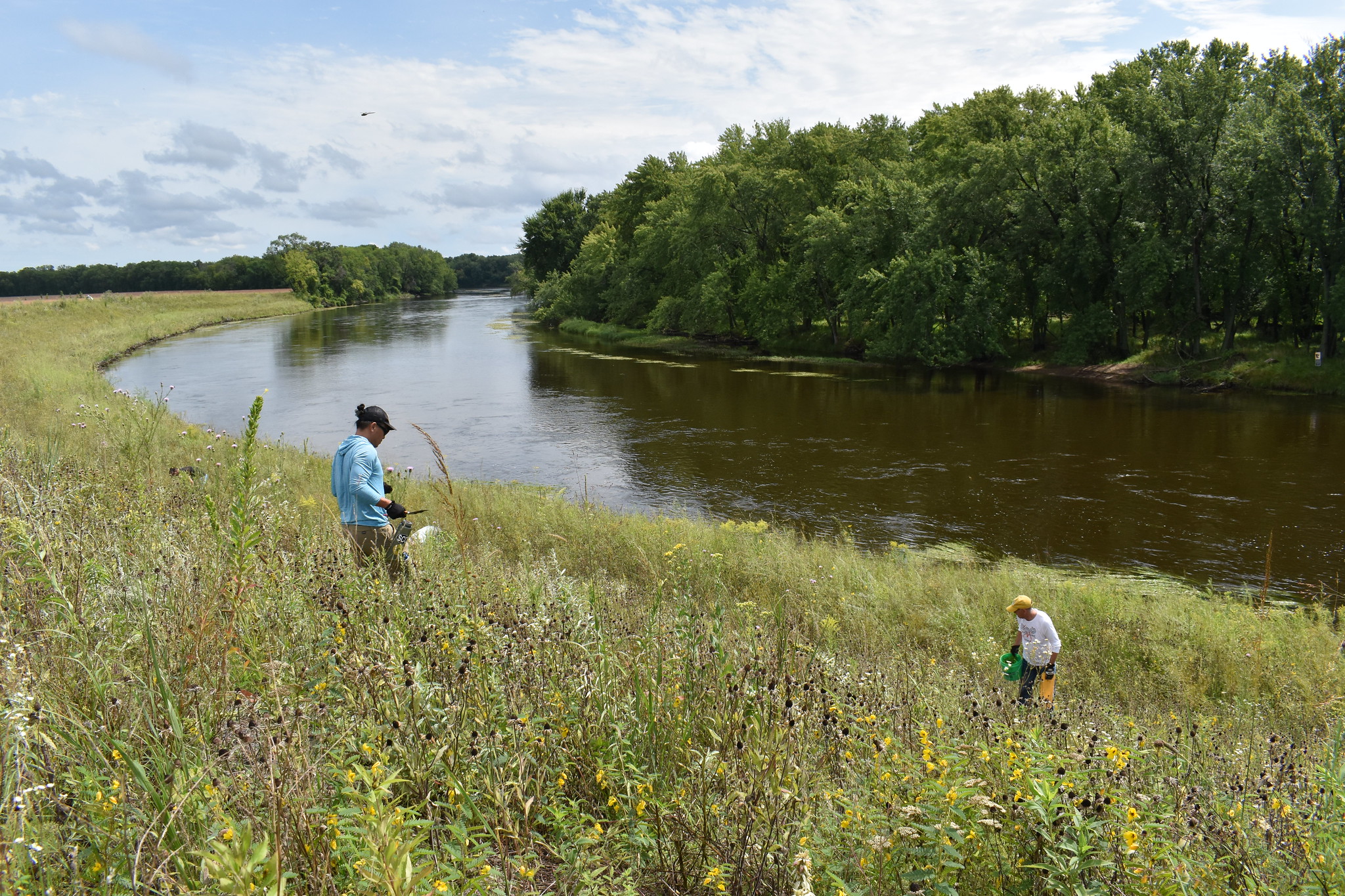 Two volunteers work in prairie by a river