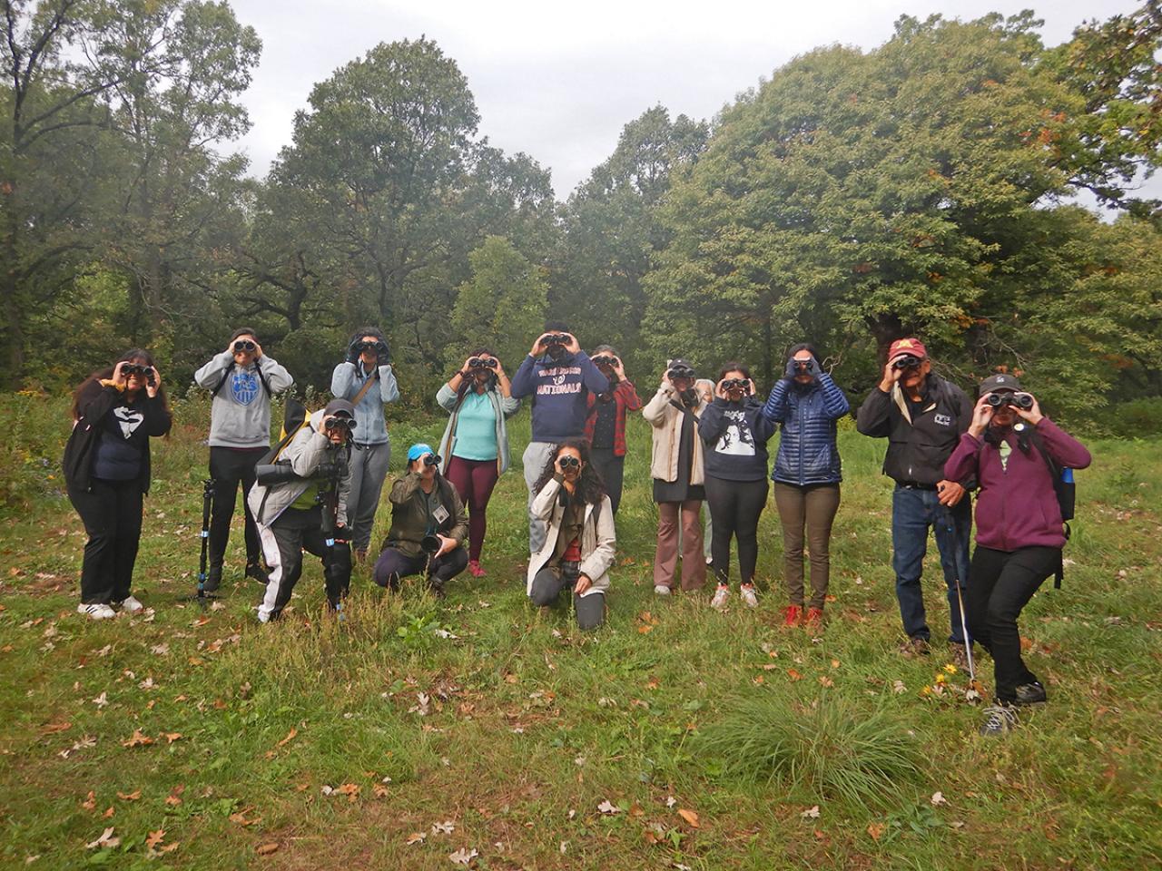 A BIPOC birding group poses, looking through binoculars