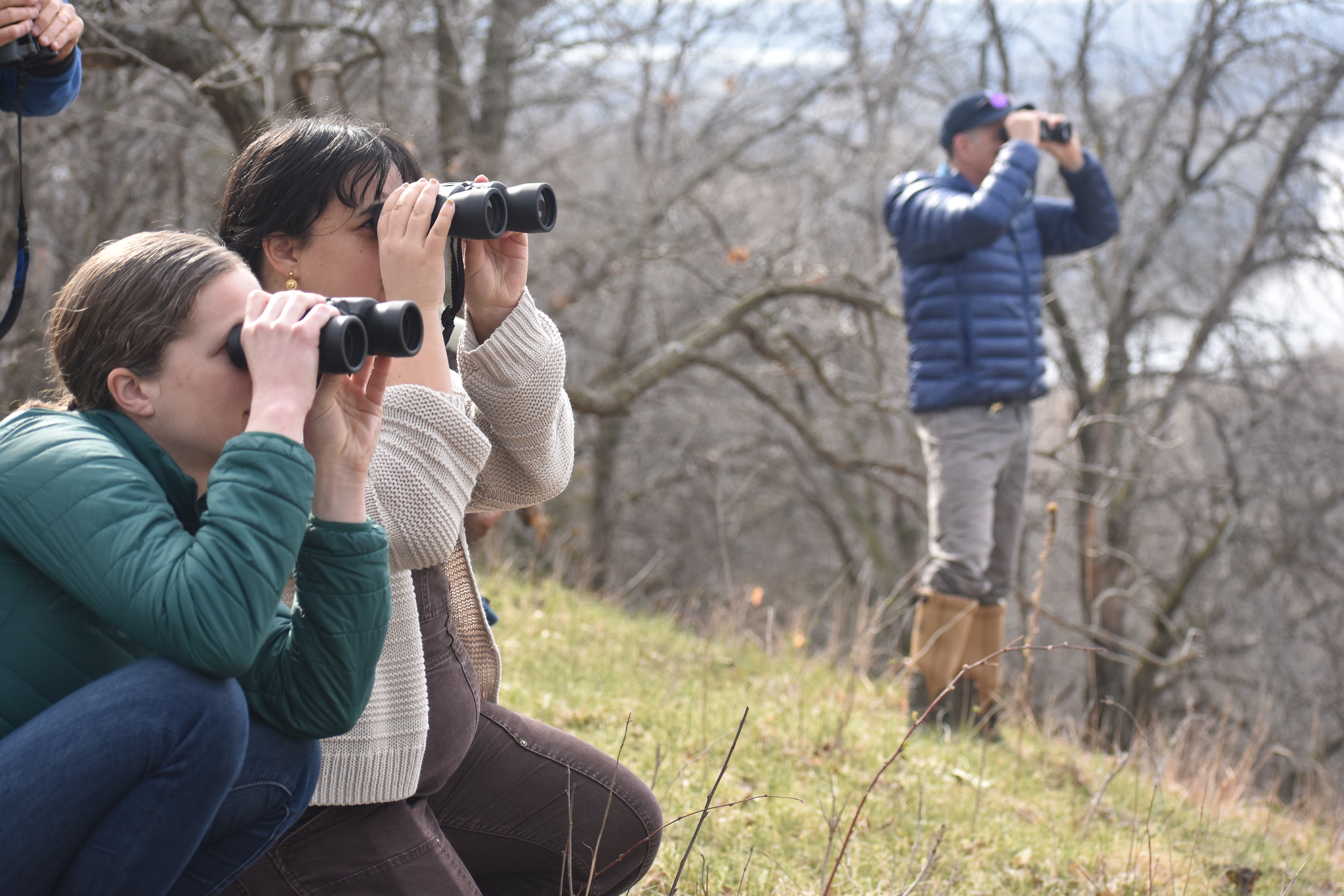 Three people stand on hillside with binoculars