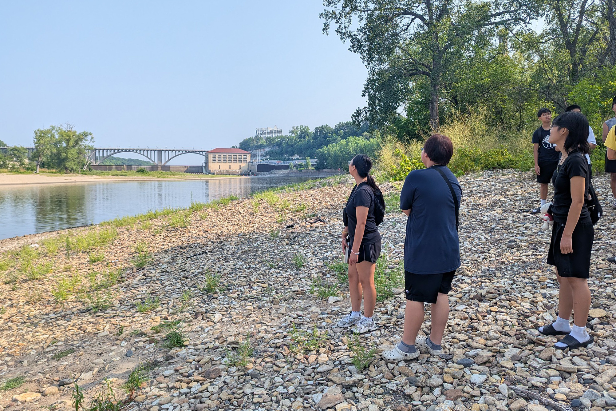 ESI summer program participants stand on the banks of the river looking at the Ford dam