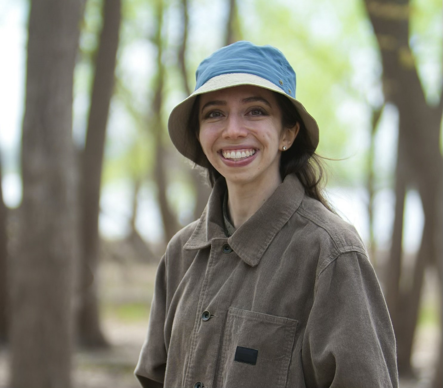 Alexandra Jabbarpour stands in a forest in early spring, green leaves and a river in the background. 
