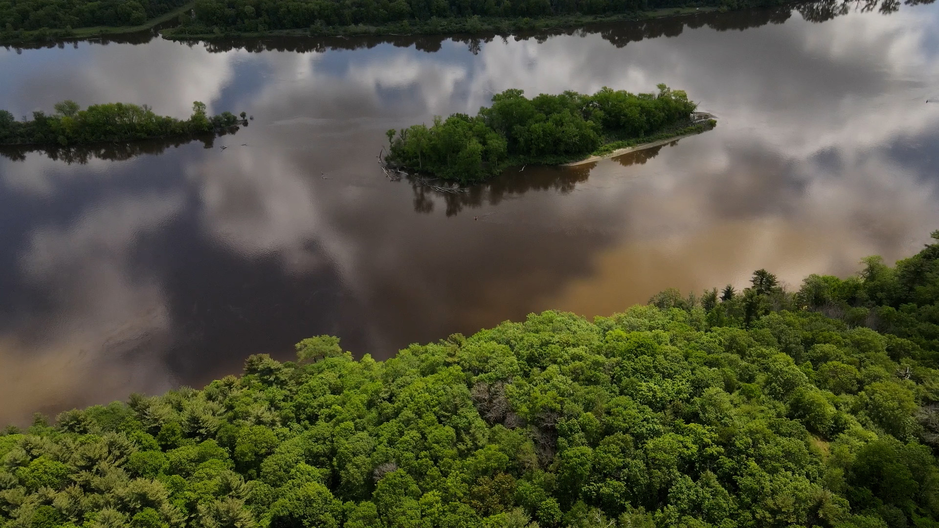 Aerial photo of forested riverbanks and river reflecting clouds