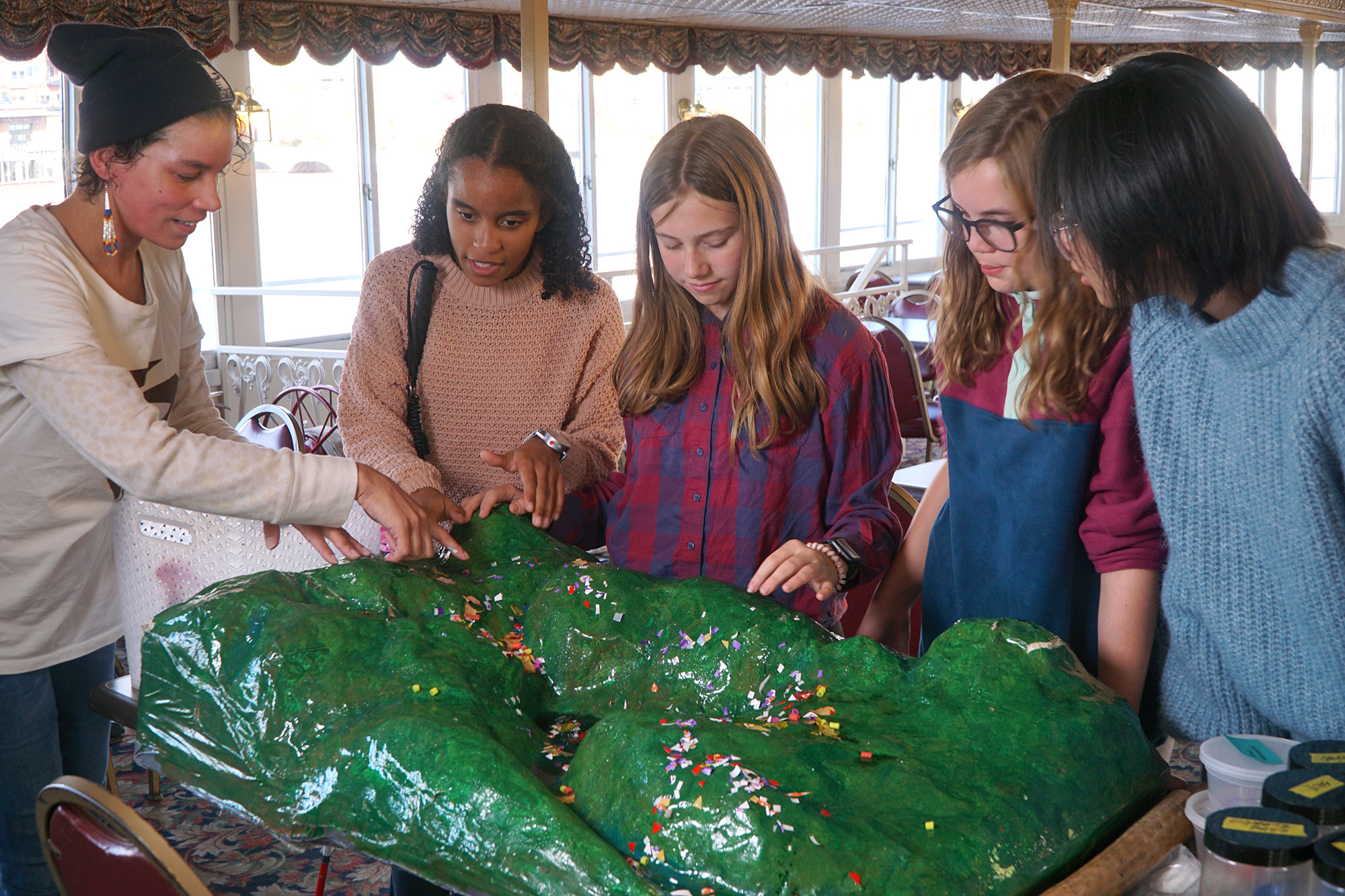 Four young people look at a watershed model with Laura 
