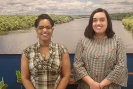 Raynette Prince and Sophie Downey stand before a large photo of the Mighty Mississippi.