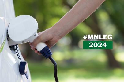A hand puts a charging plug into an electric vehicle. Text says "MN Leg 2024"