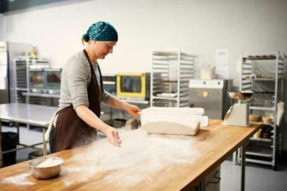 A baker at a large table, spreading flour as dough sits waiting to the side. 