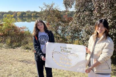 Two people stand with storm drain stencil in front of Como Lake