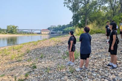 ESI summer program participants stand on the banks of the river looking at the Ford dam