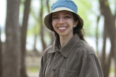 Alexandra Jabbarpour stands in a forest in early spring, green leaves and a river in the background. 