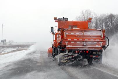 A red snow plow applying salt while traveling down a snowy road.