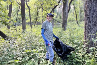 A volunteer holds a black trash bag in a forest
