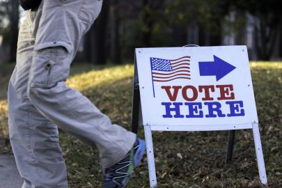 A person seen only from the waist down walks past a sign that says "Vote Here."