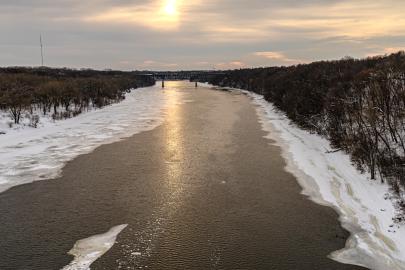 Snowy icy river with bare trees on riverbanks