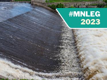 A close-up photo looking across St. Anthony Falls, as water rushes over the concrete apron and churns the river below.