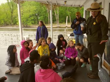 Students gather around a ranger on a boat on the Mississippi River