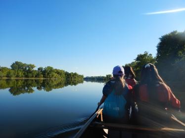 Three young people paddle a canoe on the river