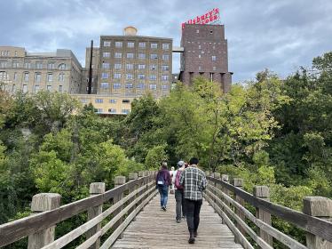 Volunteers walk across bridge toward forested area and Minneapolis buildings