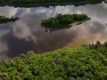 Aerial photo of forested riverbanks and river reflecting clouds