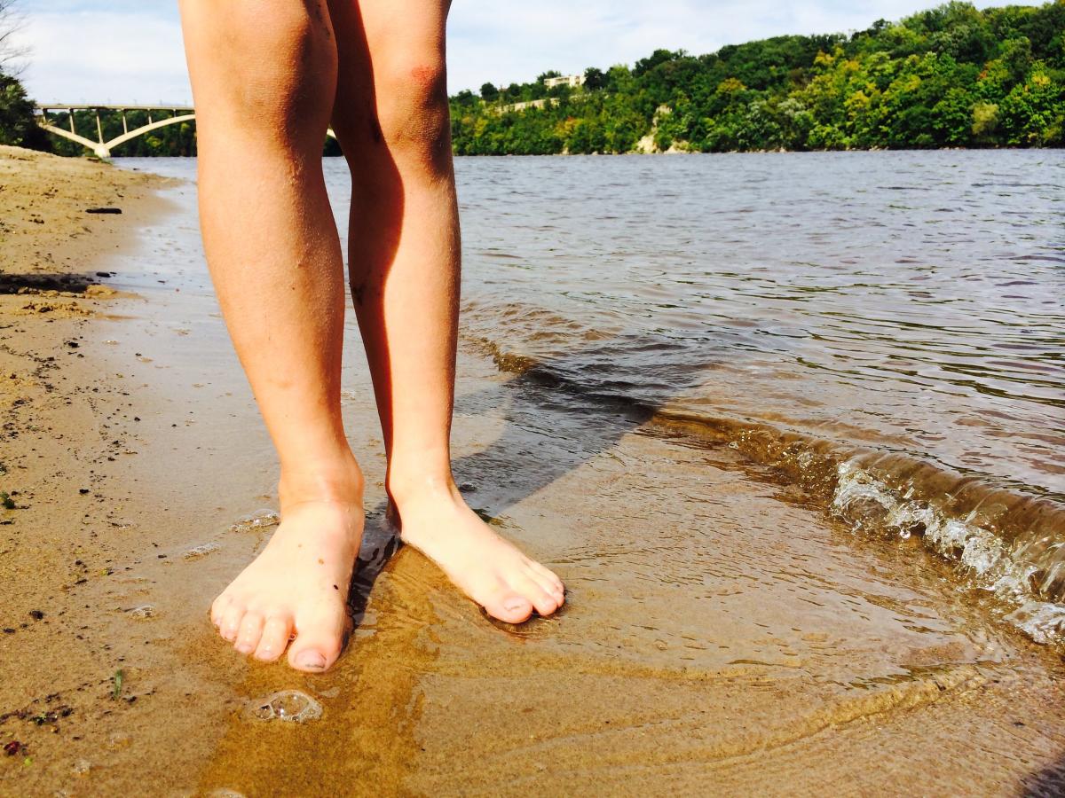 Bare feet standing on the sand along the shores of the Mississippi River in the Twin Cities.