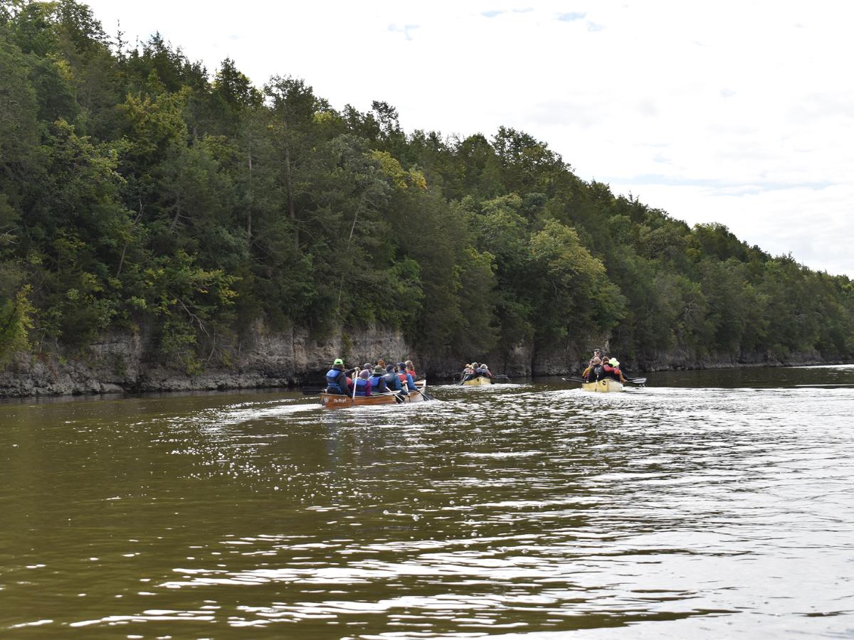 Three canoes paddle the river next to forested cliffs
