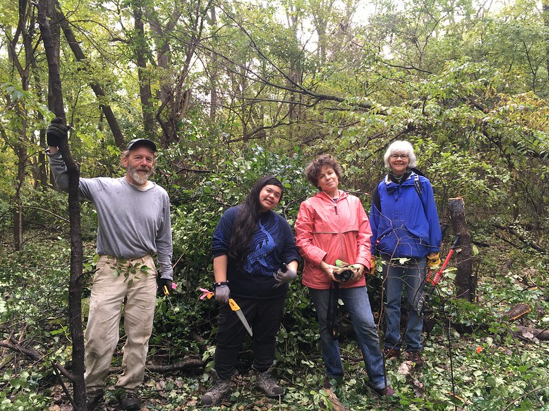 A team of four poses in front of the brush pile they've created.