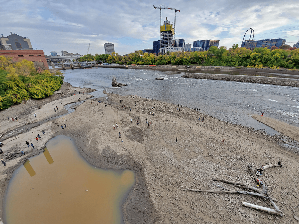 People walk on exposed riverfront in Minneapolis