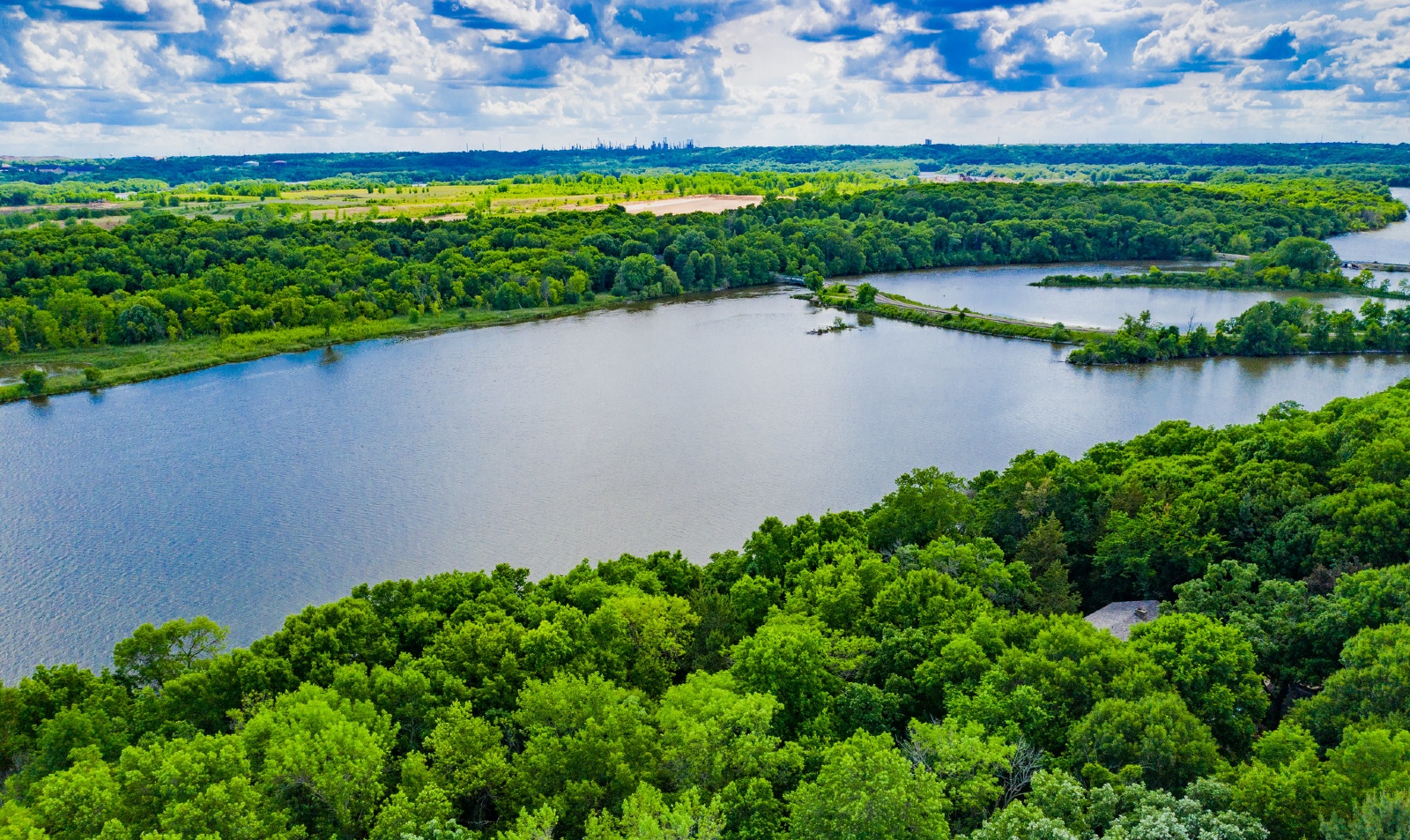 A photo looking over Mississippi Dunes, with the river in the foreground and green trees extending into the distance.