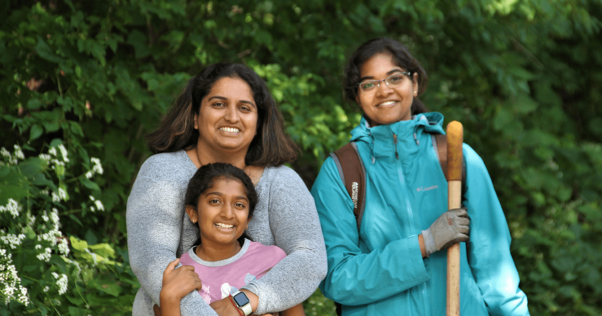 Three volunteers smile with a shovel in a forest