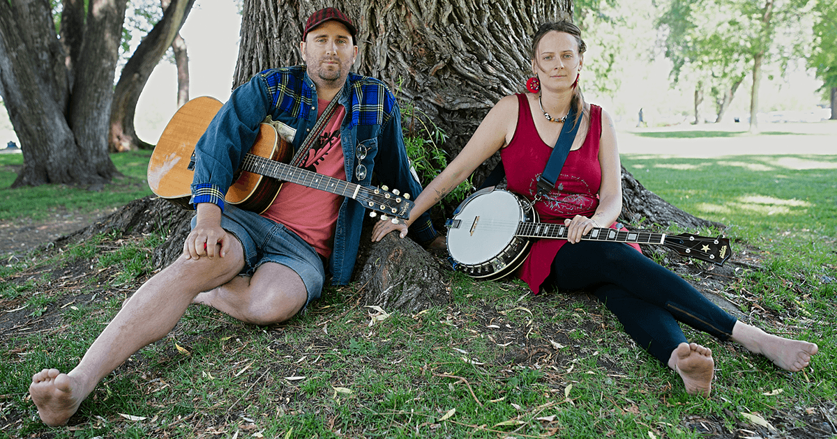 Two musicians sit by a tree